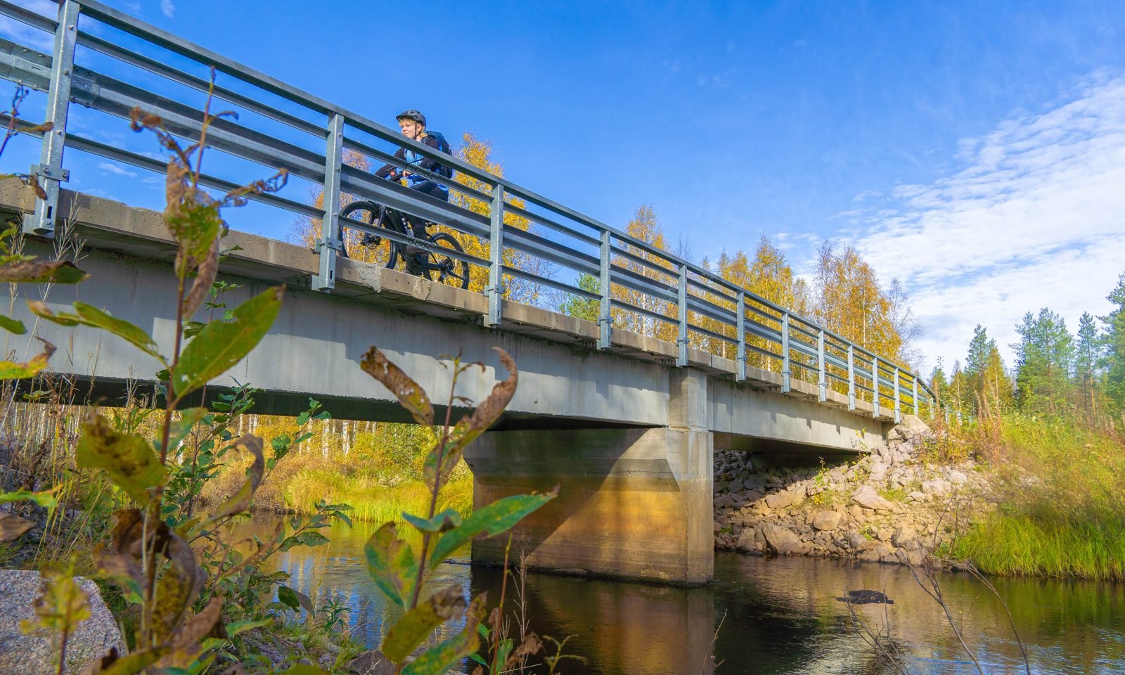 Osallistuja pyöräilee sillalla syksyisen maiseman ympäröimänä