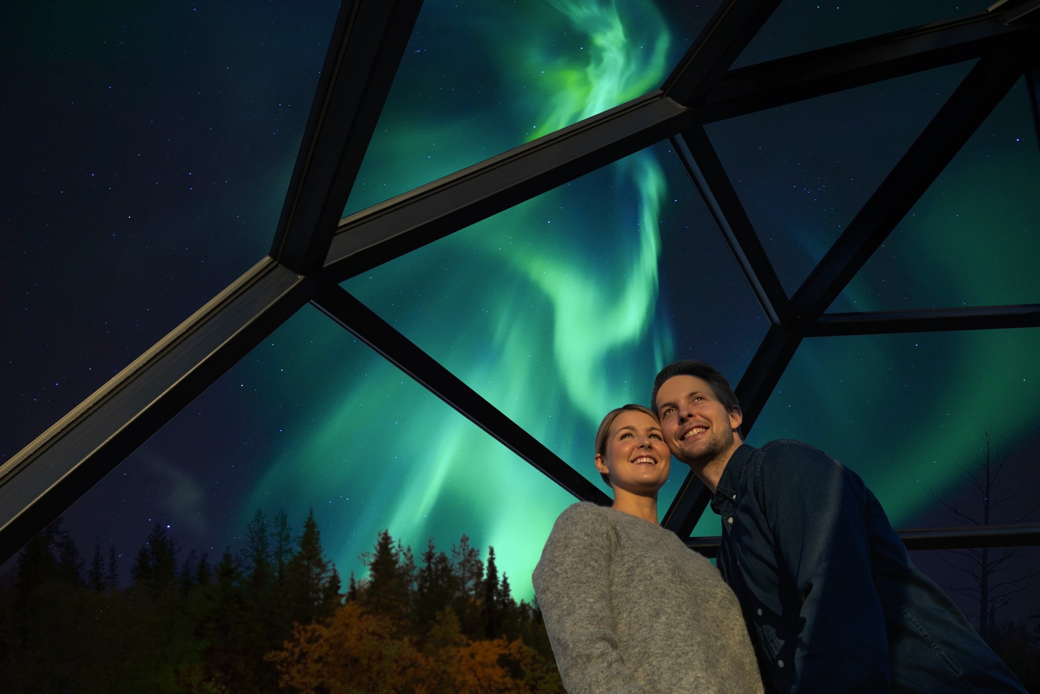 A couple in the glass igloo with Northern lights behind them