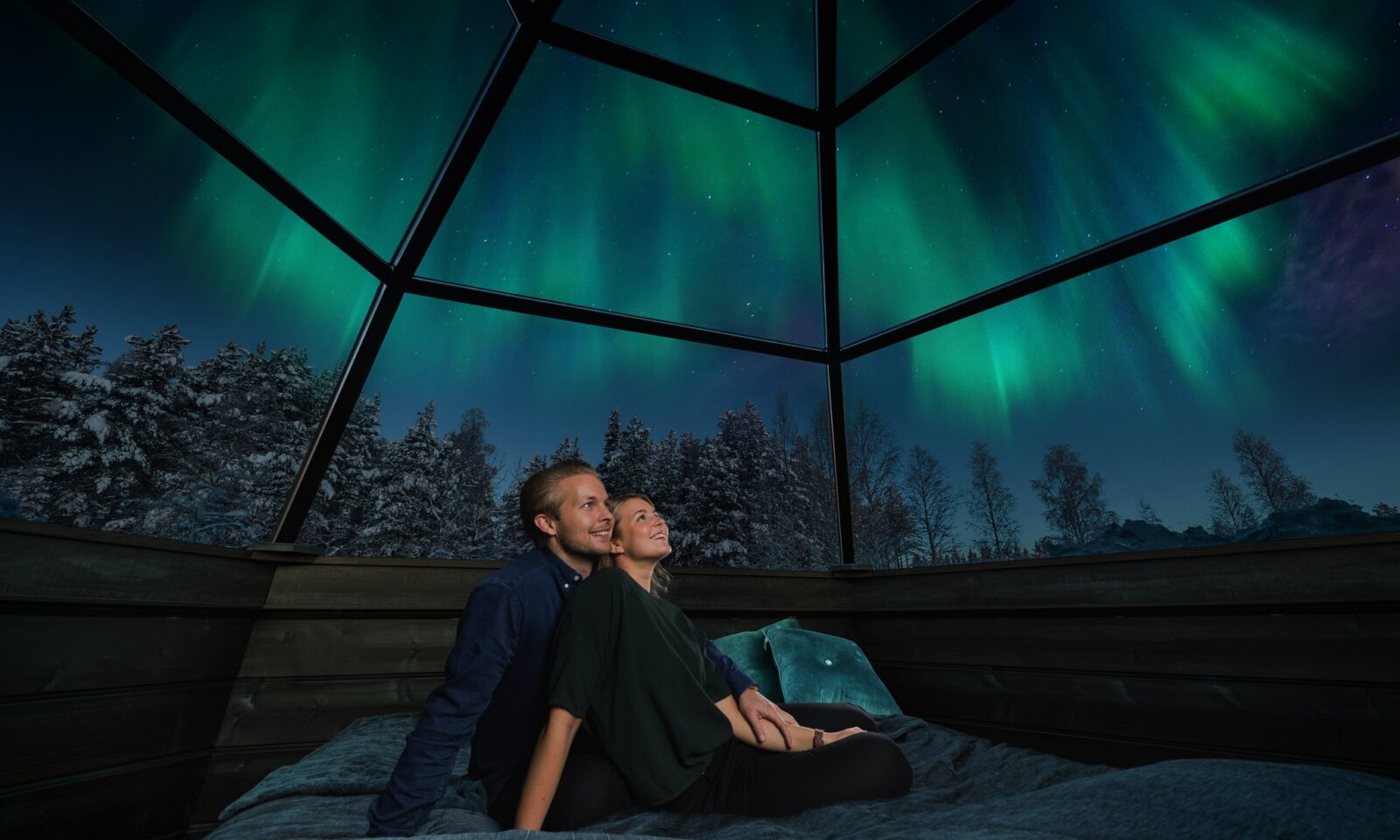 Glass Igloo Hotel in Rovaniemi: A couple sitting in a bed in Glass igloo and watching the Northern lights