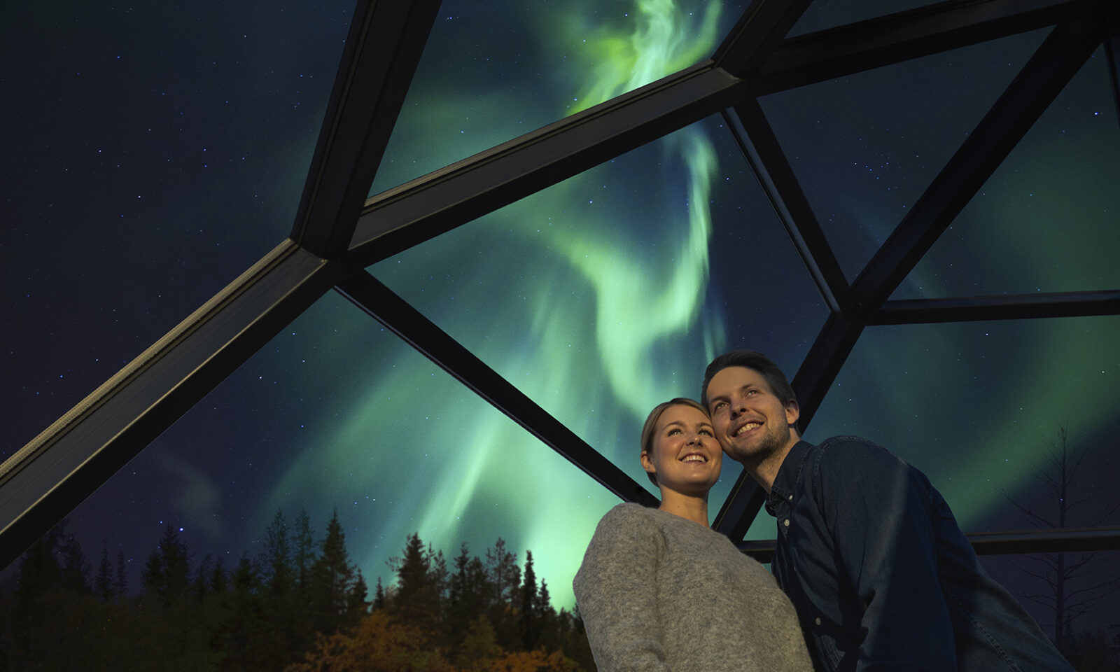 A couple in a glass igloo with northern lights in background