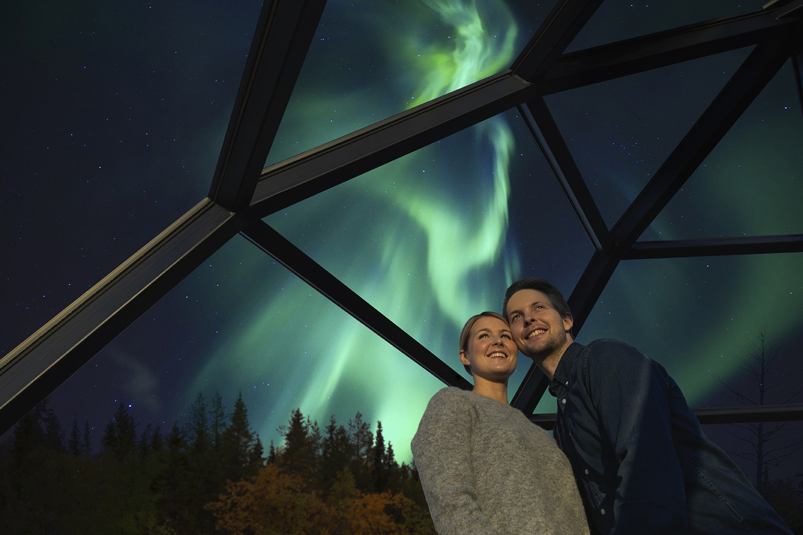 A couple in a glass igloo with northern lights in background