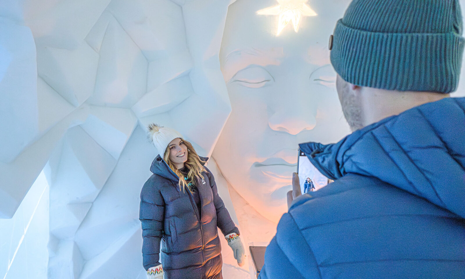 Two visitors taking photos to Instagram in front of snow art in the snow hotel