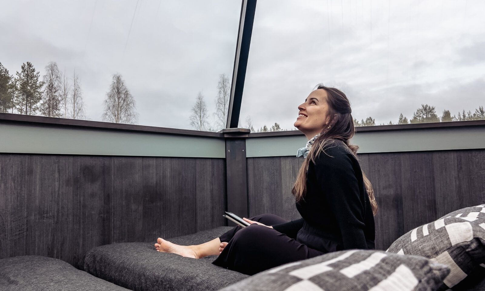 A woman sitting in a glass igloo bed in Autumn.